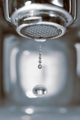 Close-up image of water droplets falling from a metal faucet.